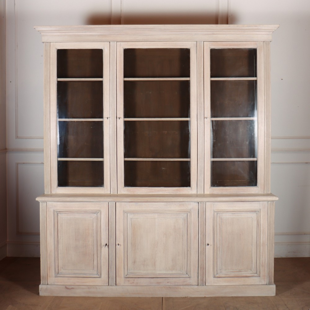 A pale English oak two-part library bookcase featuring three upper glazed doors and three lower solid panelled cupboard doors.