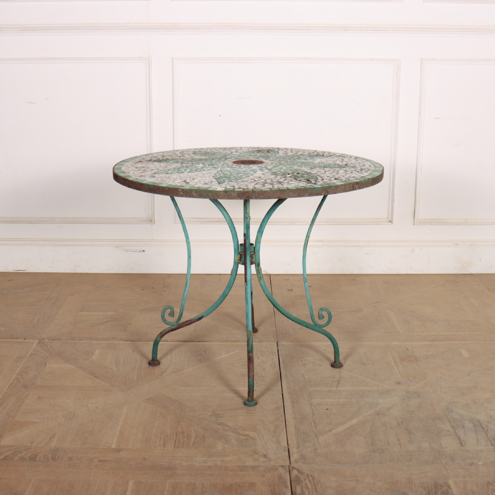 A circular garden table featuring a turquoise and off-white ceramic mosaic tile top supported by a turquoise-painted wrought iron tripod base with curved legs.