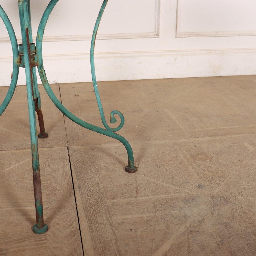 A circular garden table featuring a turquoise and off-white ceramic mosaic tile top supported by a turquoise-painted wrought iron tripod base with curved legs. View II
