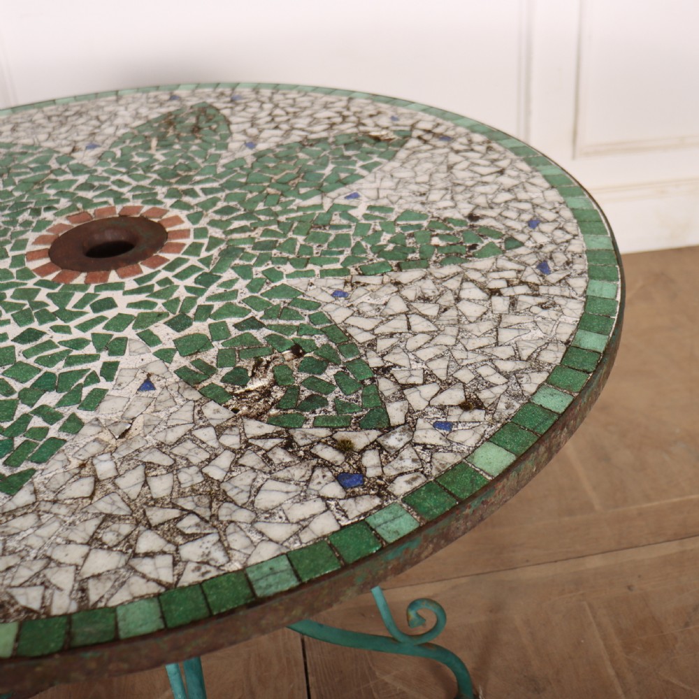 A circular garden table featuring a turquoise and off-white ceramic mosaic tile top supported by a turquoise-painted wrought iron tripod base with curved legs. View VI