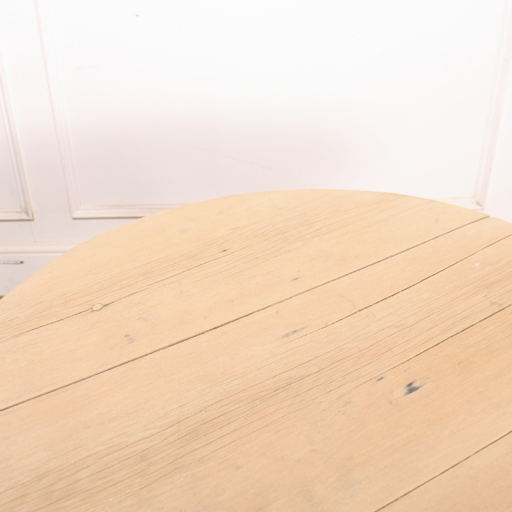A round, pale wood three-legged cricket table with a lower triangular shelf resting on a parquet floor. View V