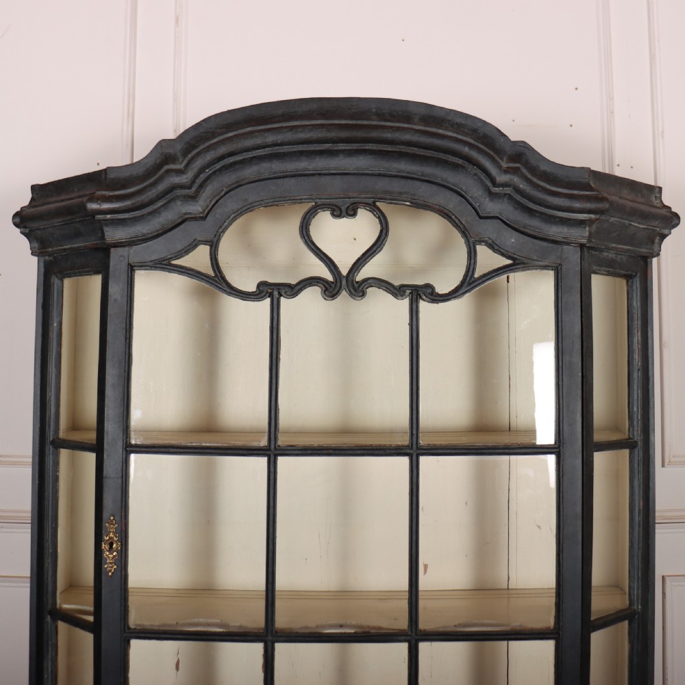 A tall, dark charcoal grey painted Dutch vitrine cabinet featuring a shaped bonnet top, glazed upper doors with curved astragal glazing bars, a cream interior, and panelled double lower doors. View II