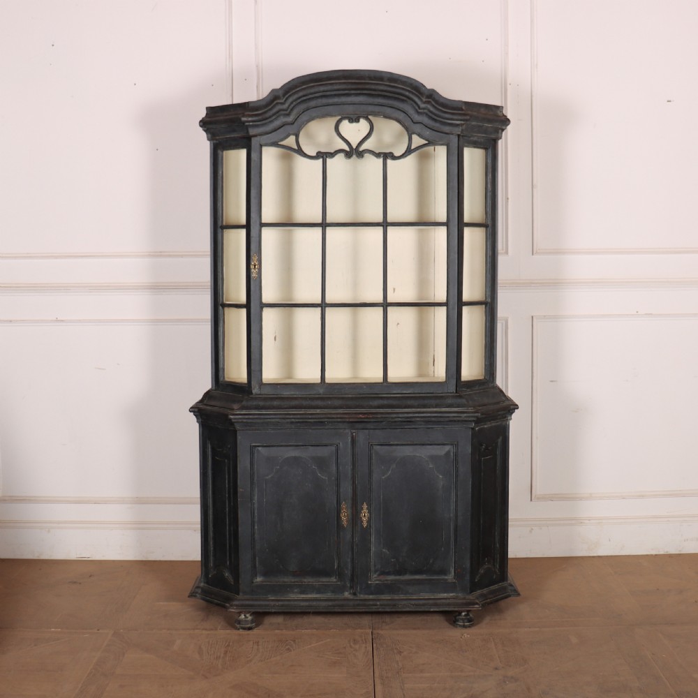 A tall, dark charcoal grey painted Dutch vitrine cabinet featuring a shaped bonnet top, glazed upper doors with curved astragal glazing bars, a cream interior, and panelled double lower doors. View III