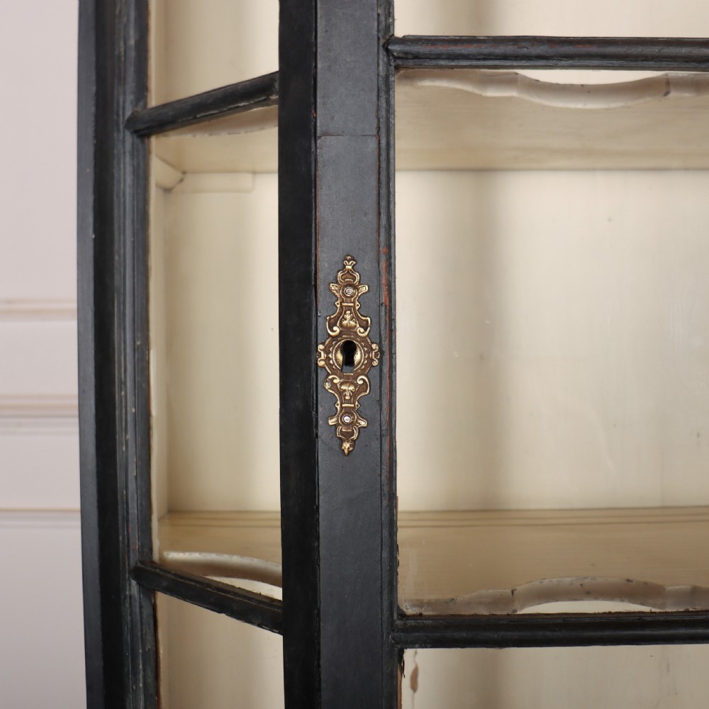 A tall, dark charcoal grey painted Dutch vitrine cabinet featuring a shaped bonnet top, glazed upper doors with curved astragal glazing bars, a cream interior, and panelled double lower doors. View IV