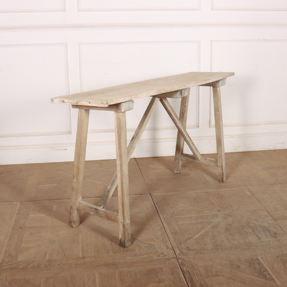 A long, narrow antique French rustic wooden trestle table with a weathered pale finish and diagonal cross-bracing.