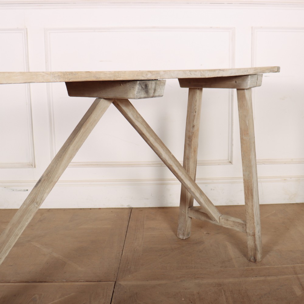 A long, narrow antique French rustic wooden trestle table with a weathered pale finish and diagonal cross-bracing. View IV
