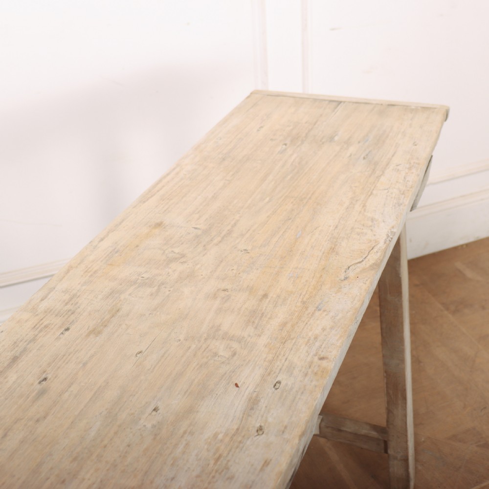 A long, narrow antique French rustic wooden trestle table with a weathered pale finish and diagonal cross-bracing. View V