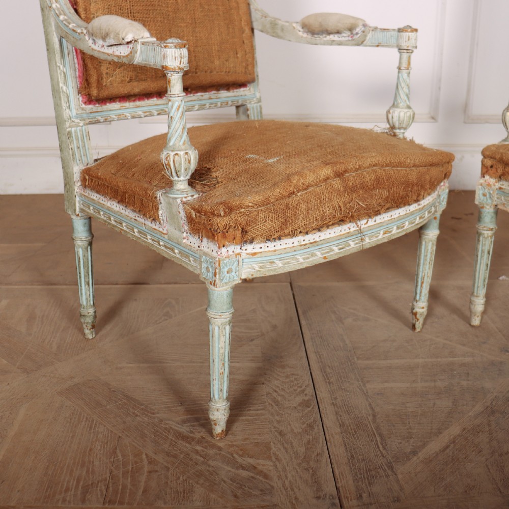A pair of antique French Louis XVI open armchairs featuring carved, distressed light blue painted frames, fluted legs, and exposed hessian upholstery. View II