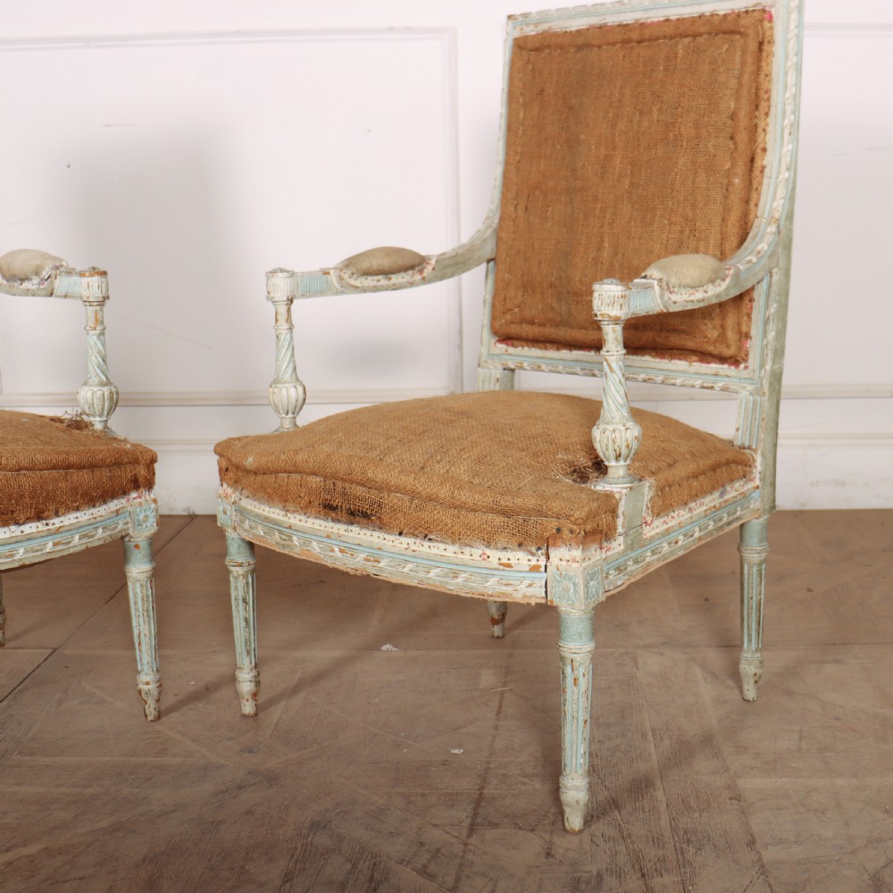 A pair of antique French Louis XVI open armchairs featuring carved, distressed light blue painted frames, fluted legs, and exposed hessian upholstery. View V
