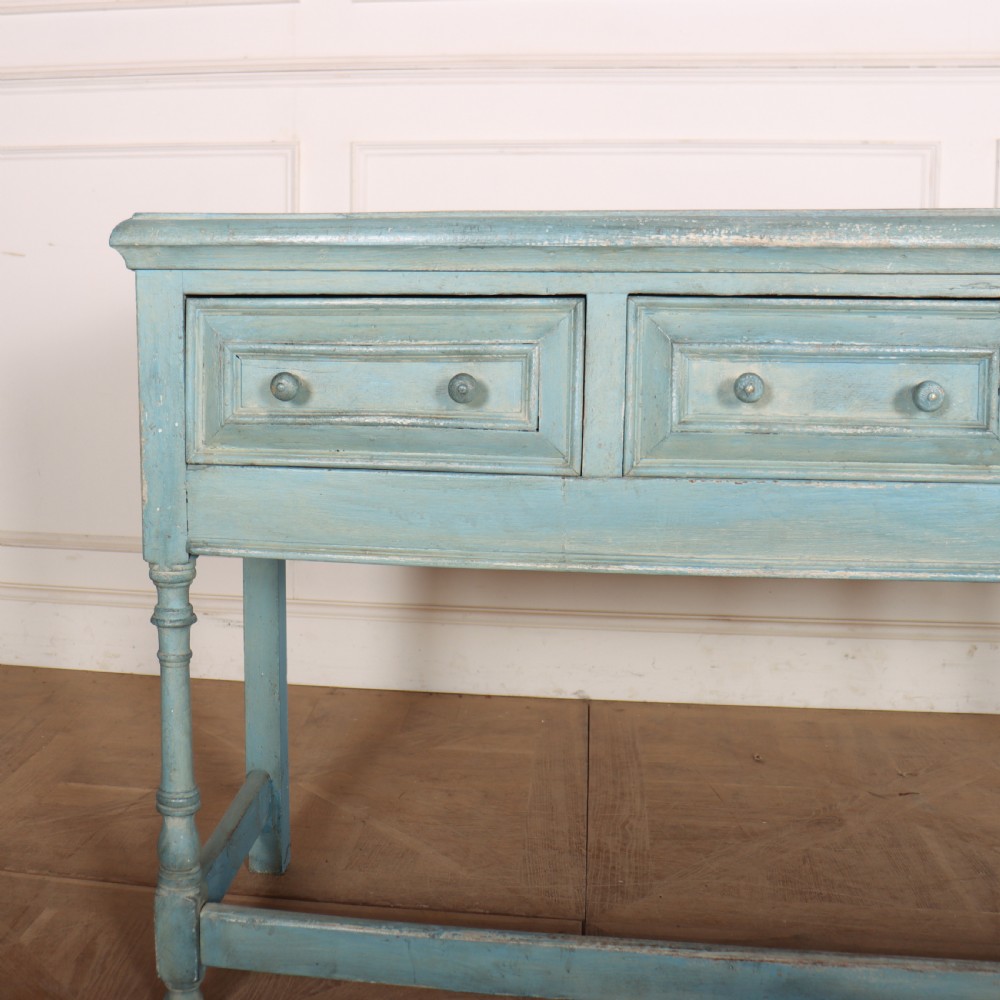 A pale blue painted wooden dresser base featuring three inline drawers with small wooden knobs and turned front legs connected by a low stretcher. View III