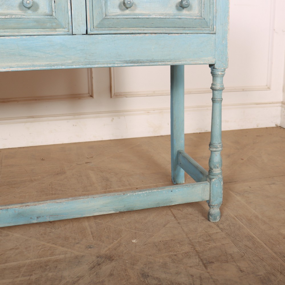A pale blue painted wooden dresser base featuring three inline drawers with small wooden knobs and turned front legs connected by a low stretcher. View V