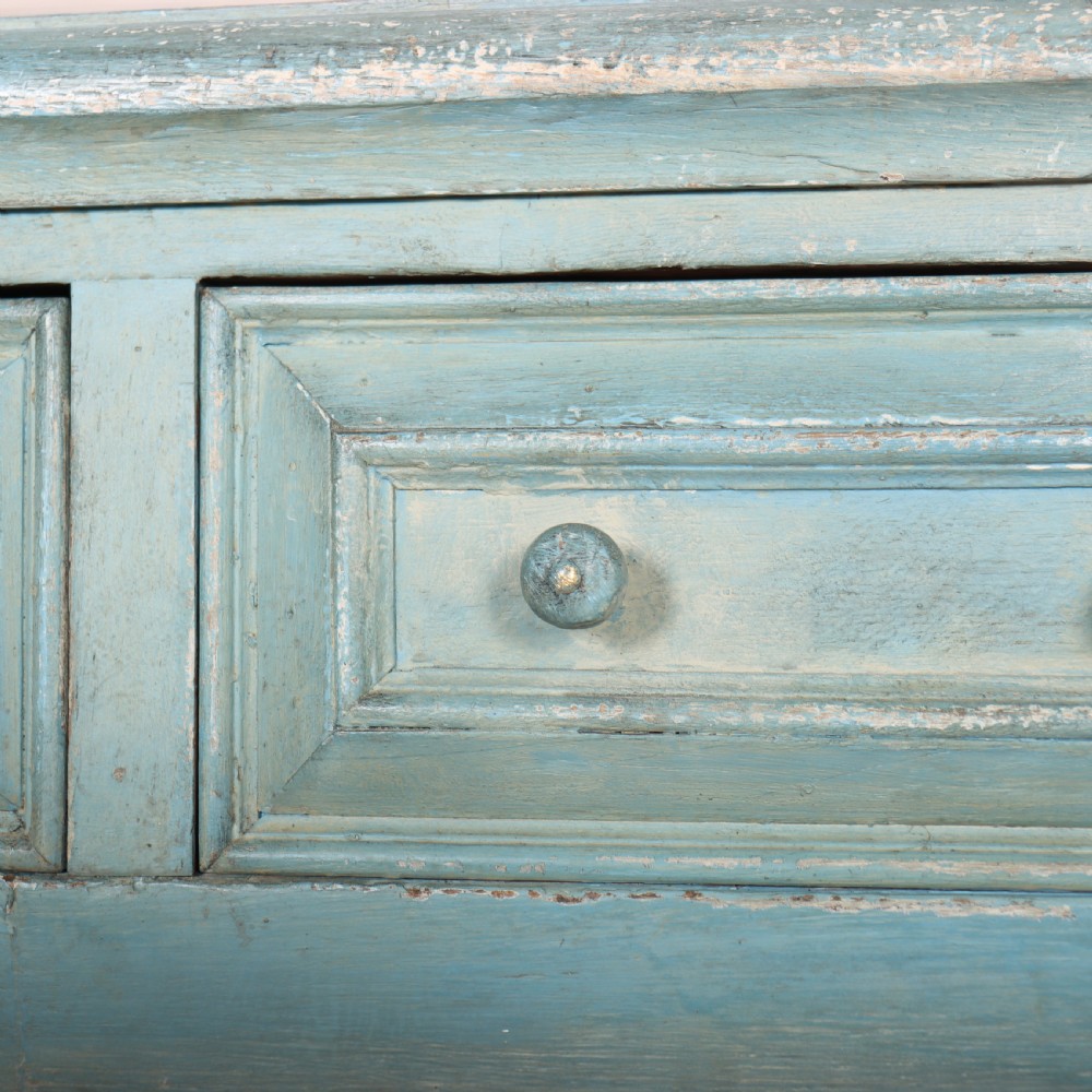 A pale blue painted wooden dresser base featuring three inline drawers with small wooden knobs and turned front legs connected by a low stretcher. View VIII