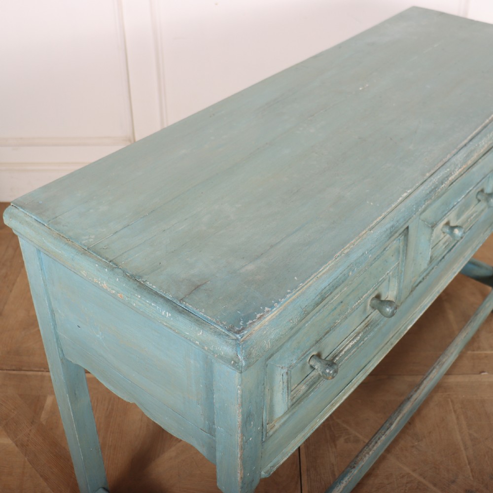 A pale blue painted wooden dresser base featuring three inline drawers with small wooden knobs and turned front legs connected by a low stretcher. View XI