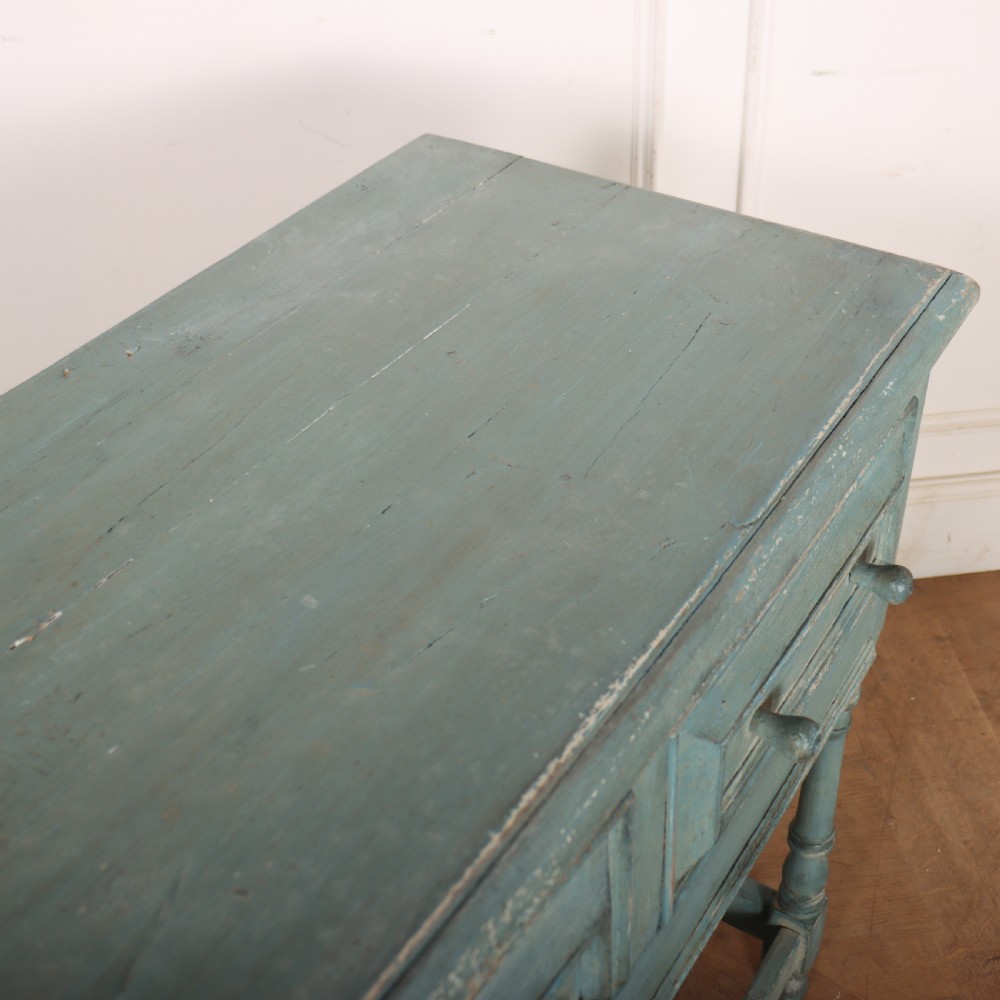 A pale blue painted wooden dresser base featuring three inline drawers with small wooden knobs and turned front legs connected by a low stretcher. View XII