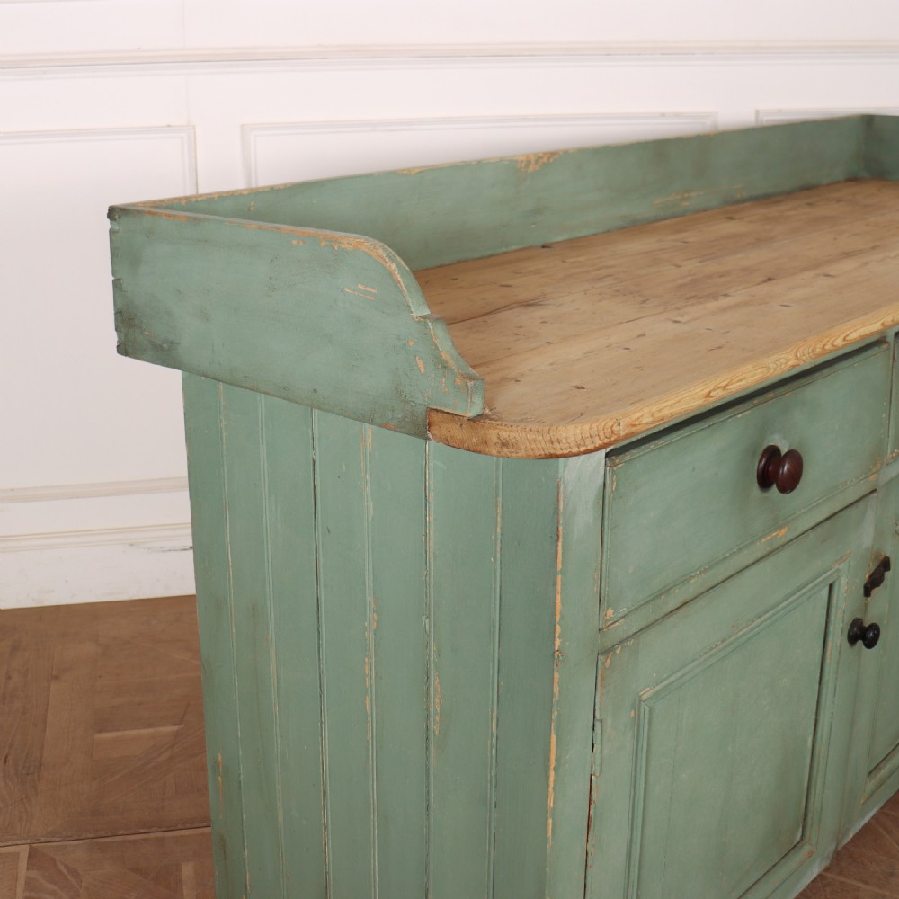 A Scottish antique pine dairy dresser featuring a sage green painted body with three drawers over three cupboard doors and a scrubbed pine top. View II