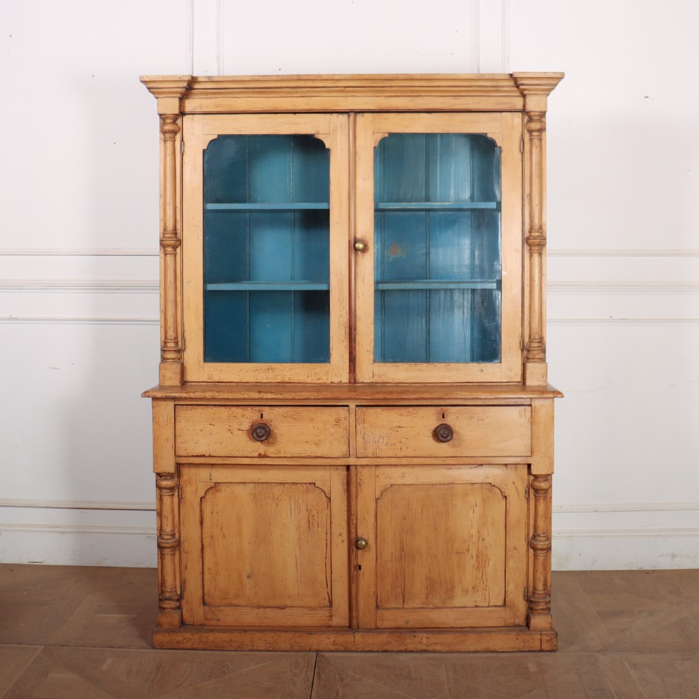 An antique pine glazed dresser with two upper glazed doors revealing a vibrant blue interior above two drawers and two cabinet doors.