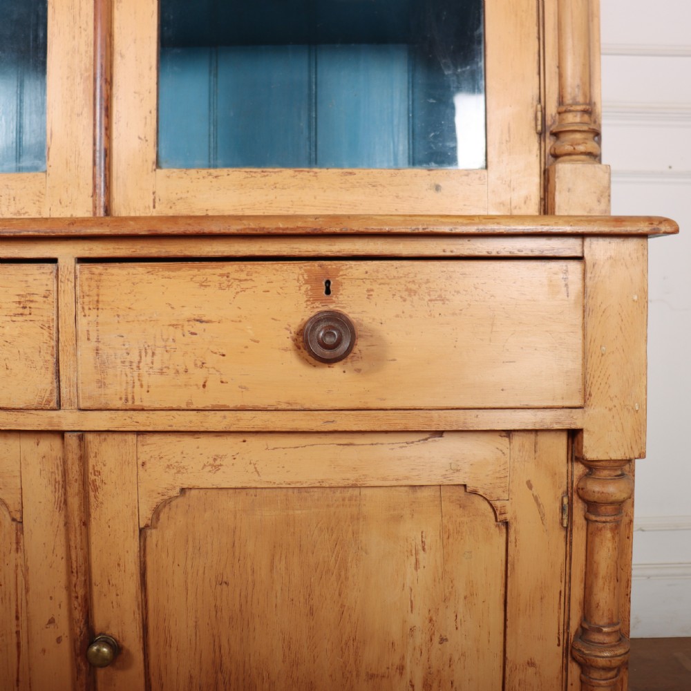 A two-tier antique pine glazed dresser with a blue painted interior, turned corner columns, two drawers, and two lower wooden cabinet doors. View VII