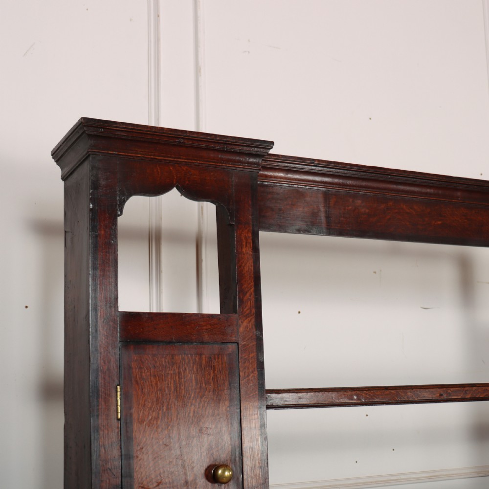 An 18th-century dark oak dresser featuring an open upper plate rack flanked by narrow side cupboards over a base with three drawers and a scalloped apron. View II