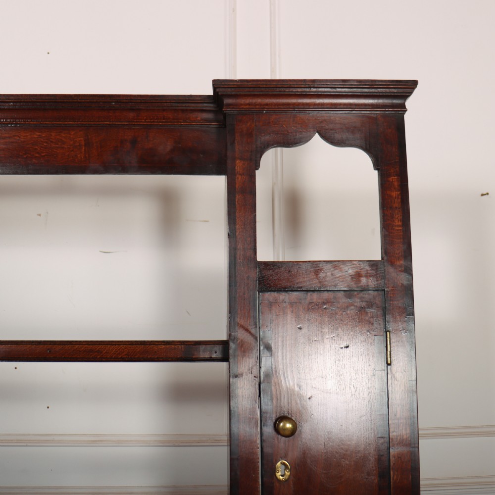 An 18th-century dark oak dresser featuring an open upper plate rack flanked by narrow side cupboards over a base with three drawers and a scalloped apron. View III