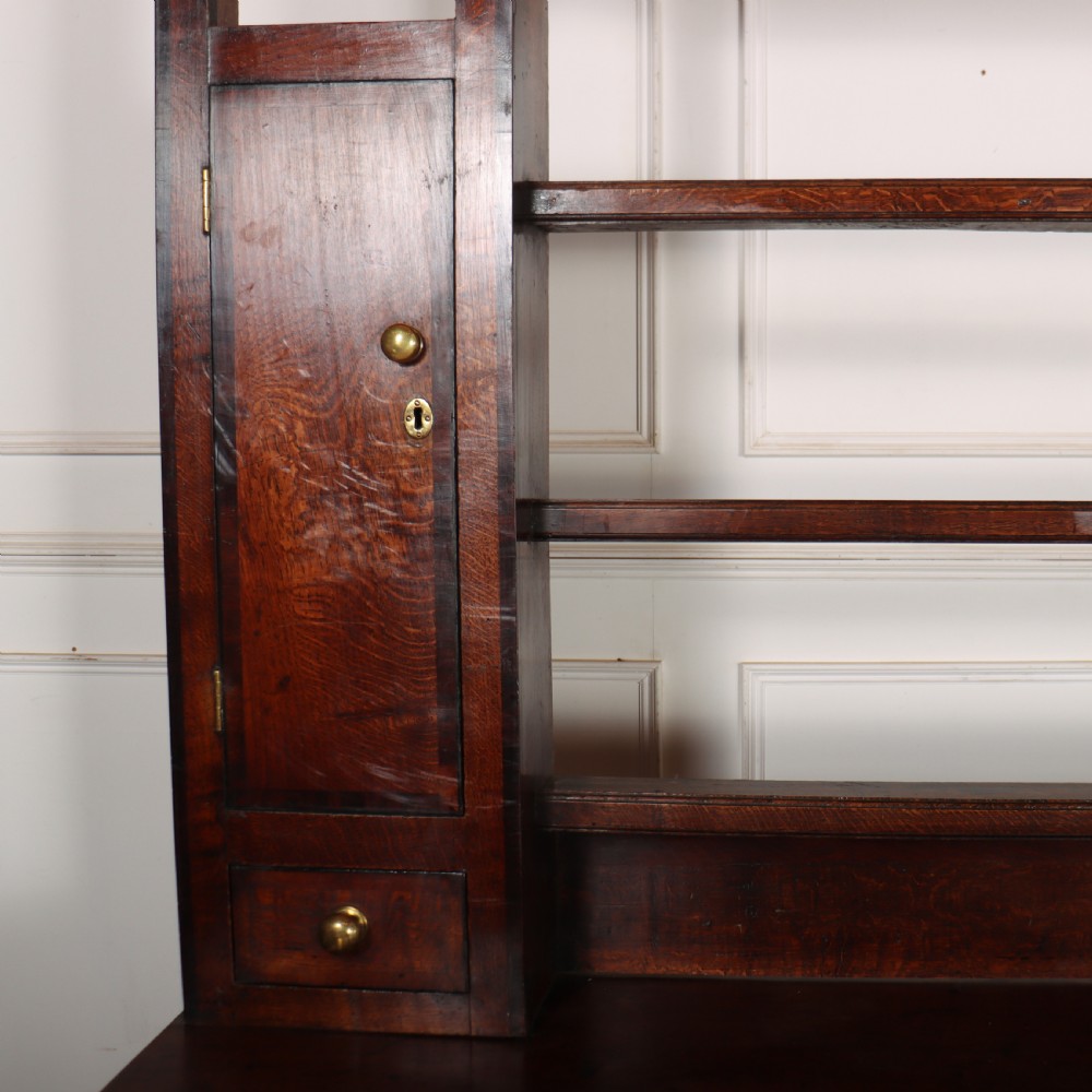 An 18th-century dark oak dresser featuring an open upper plate rack flanked by narrow side cupboards over a base with three drawers and a scalloped apron. View IV