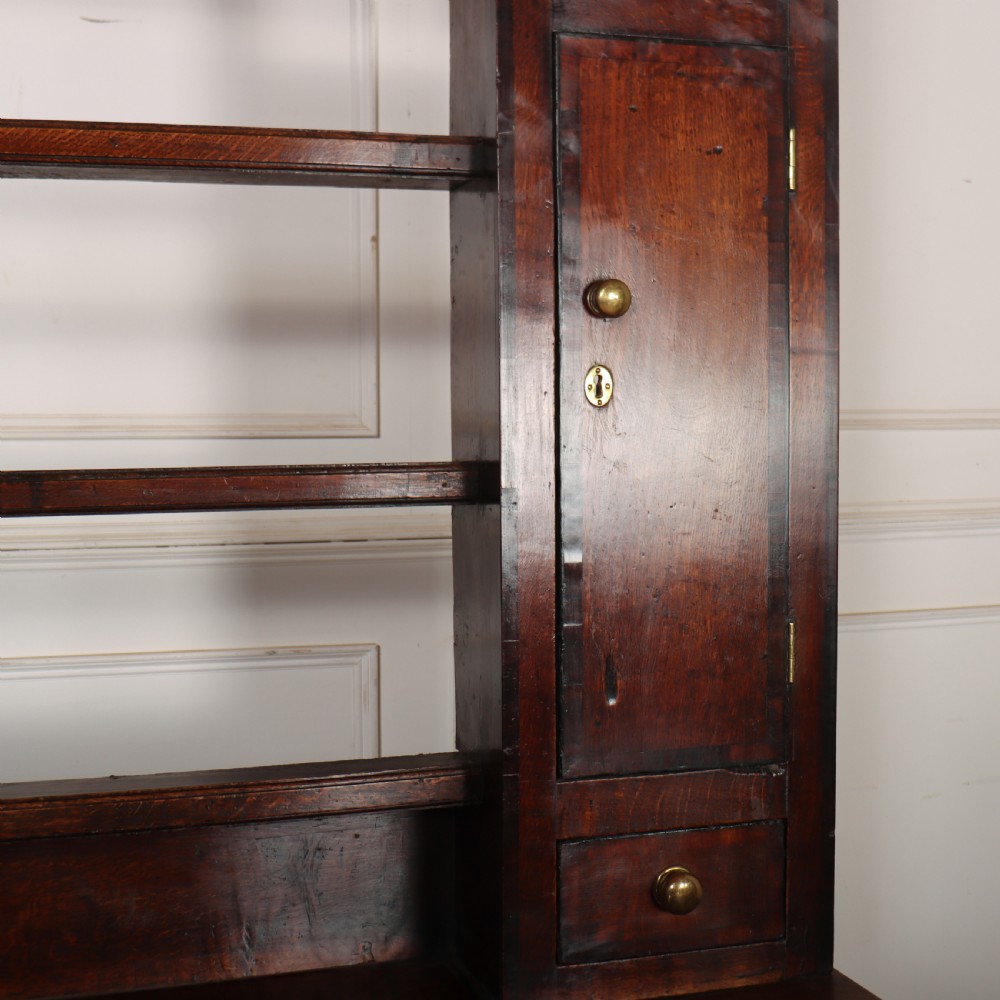An 18th-century dark oak dresser featuring an open upper plate rack flanked by narrow side cupboards over a base with three drawers and a scalloped apron. View V