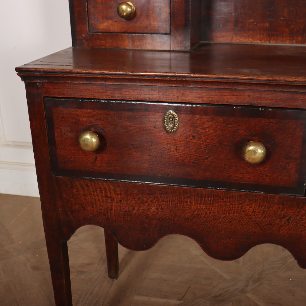 An 18th-century dark oak dresser featuring an open upper plate rack flanked by narrow side cupboards over a base with three drawers and a scalloped apron. View VI