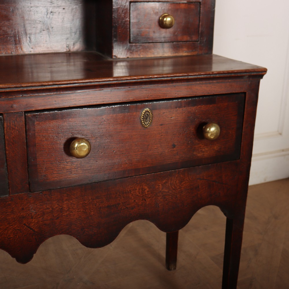 An 18th-century dark oak dresser featuring an open upper plate rack flanked by narrow side cupboards over a base with three drawers and a scalloped apron. View VIII