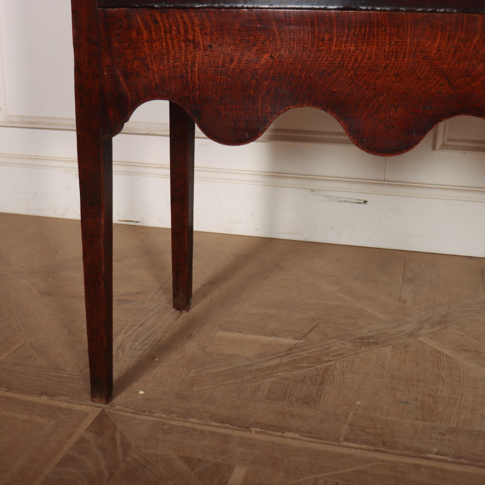An 18th-century dark oak dresser featuring an open upper plate rack flanked by narrow side cupboards over a base with three drawers and a scalloped apron. View IX