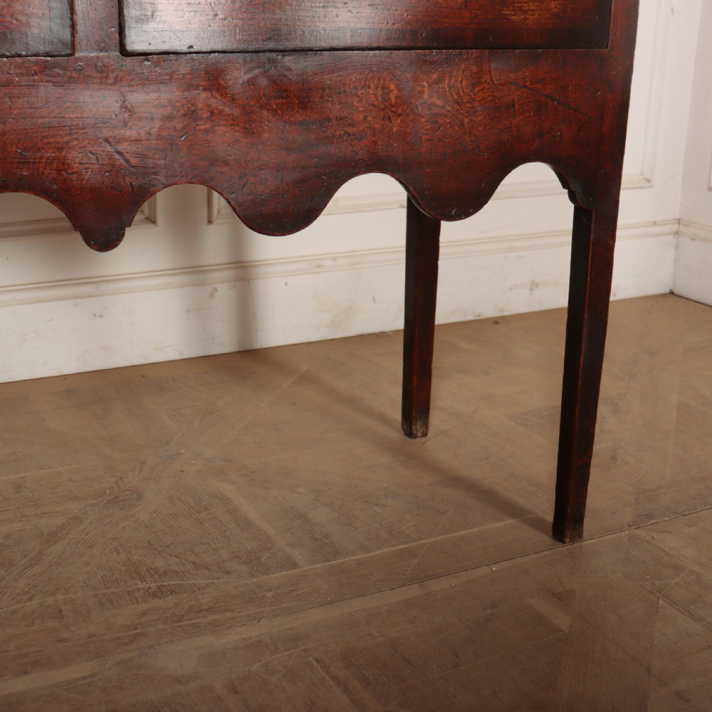 An 18th-century dark oak dresser featuring an open upper plate rack flanked by narrow side cupboards over a base with three drawers and a scalloped apron. View X