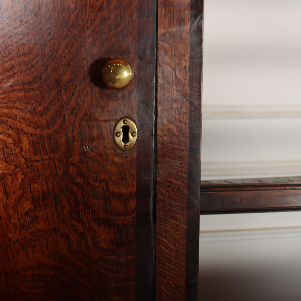 An 18th-century dark oak dresser featuring an open upper plate rack flanked by narrow side cupboards over a base with three drawers and a scalloped apron. View XI
