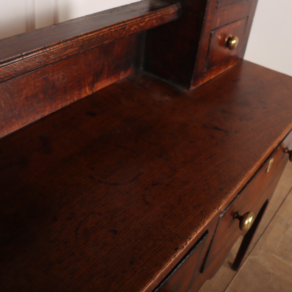 An 18th-century dark oak dresser featuring an open upper plate rack flanked by narrow side cupboards over a base with three drawers and a scalloped apron. View XIII