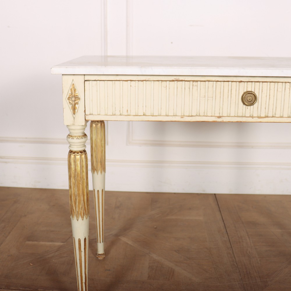 An off-white painted Swedish side table featuring a white marble top, fluted frieze with a central drawer knob, and tapered fluted legs with gilded accents. View III