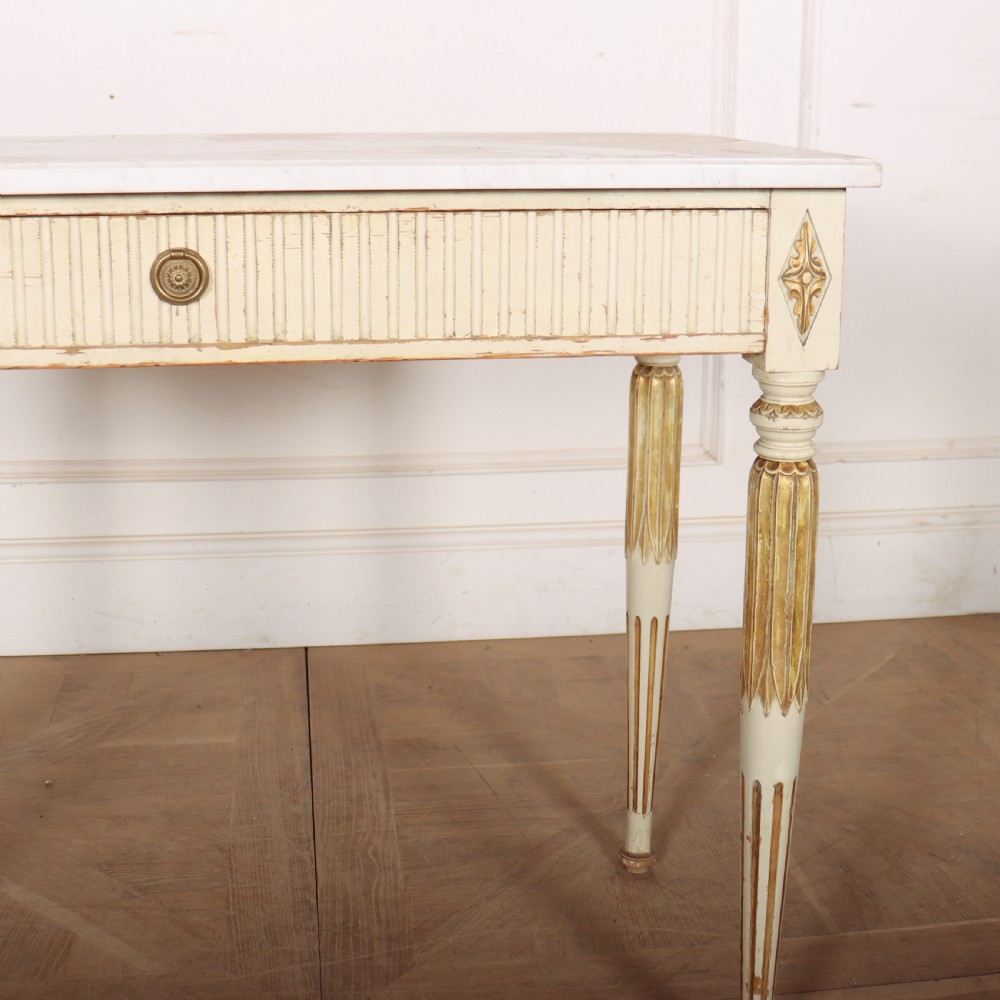 An off-white painted Swedish side table featuring a white marble top, fluted frieze with a central drawer knob, and tapered fluted legs with gilded accents. View V