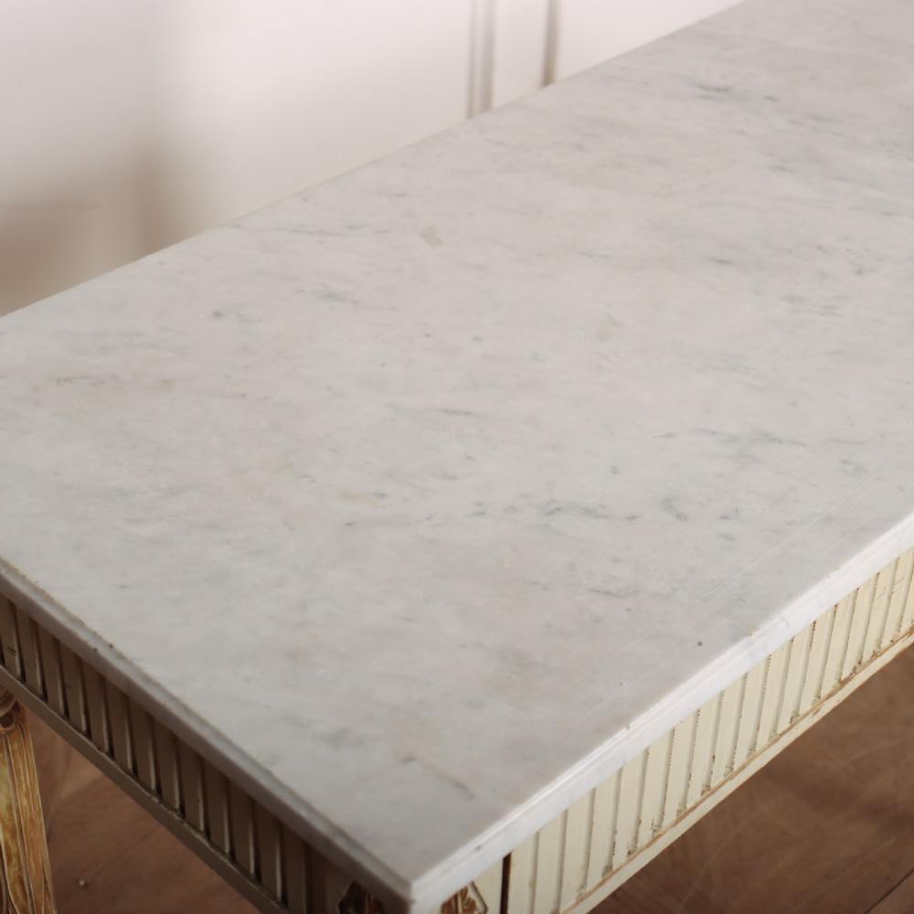 An off-white painted Swedish side table featuring a white marble top, fluted frieze with a central drawer knob, and tapered fluted legs with gilded accents. View VIII