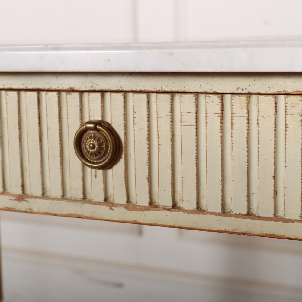 An off-white painted Swedish side table featuring a white marble top, fluted frieze with a central drawer knob, and tapered fluted legs with gilded accents. View XI