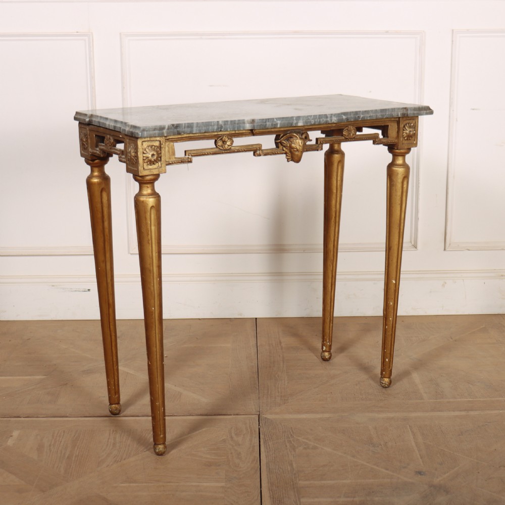 A rectangular gilded console table featuring a grey marble top, carved rams head central motif, rosettes, and tapered legs.