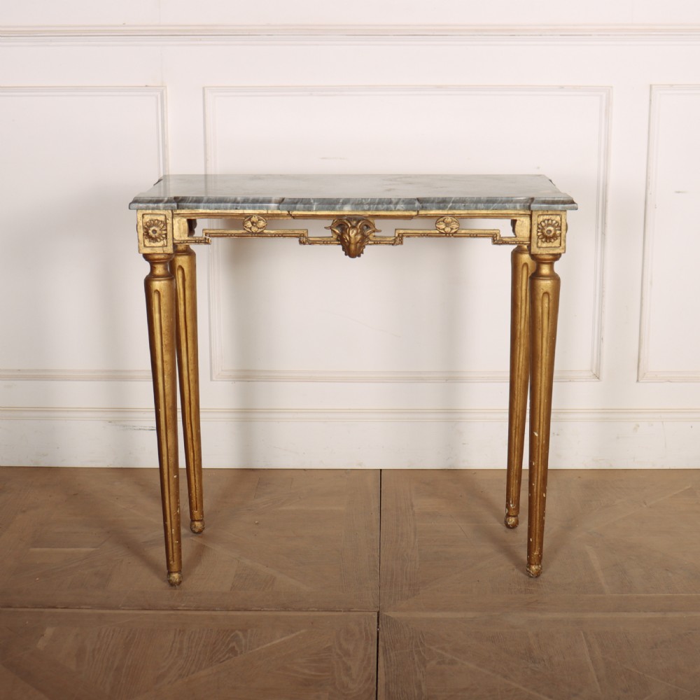A rectangular gilded console table featuring a grey marble top, carved rams head central motif, rosettes, and tapered legs. View II