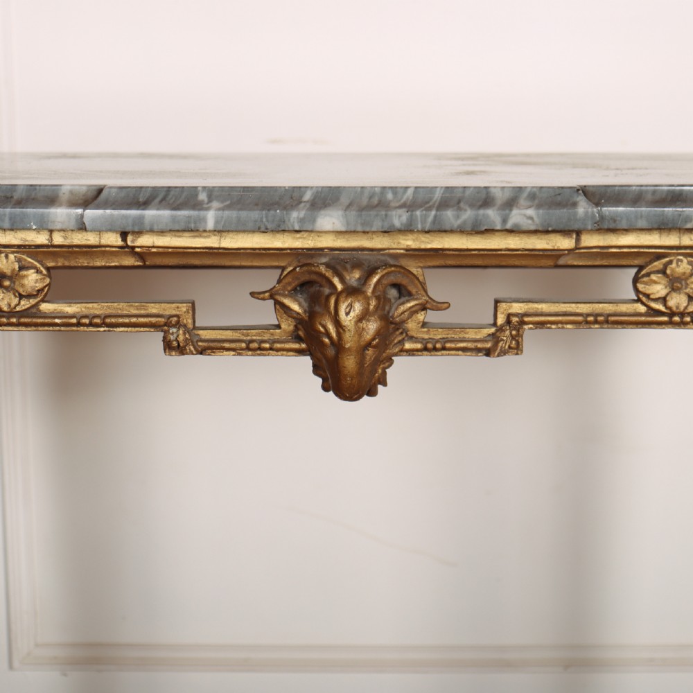 A rectangular gilded console table featuring a grey marble top, carved rams head central motif, rosettes, and tapered legs. View VI