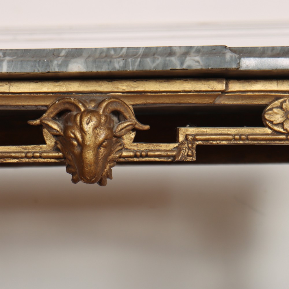 A rectangular gilded console table featuring a grey marble top, carved rams head central motif, rosettes, and tapered legs. View VIII