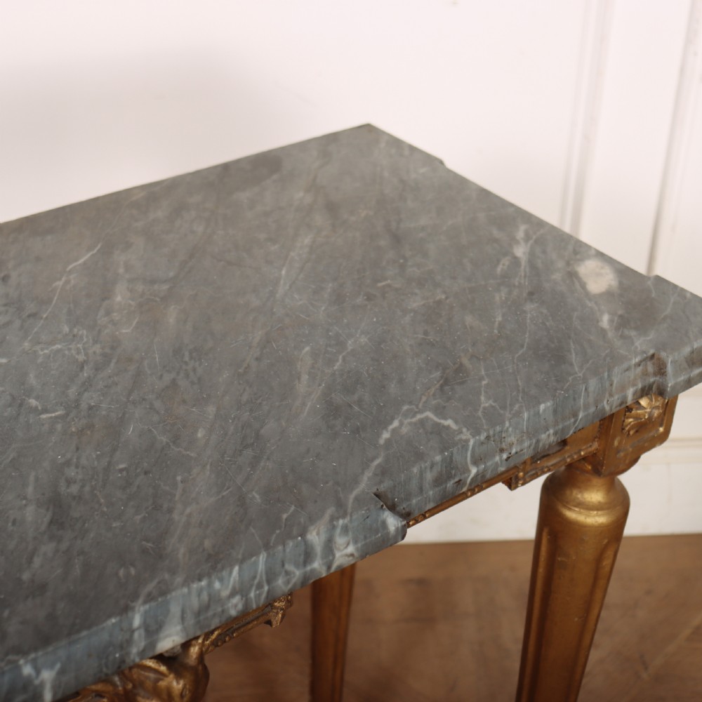 A rectangular gilded console table featuring a grey marble top, carved rams head central motif, rosettes, and tapered legs. View X