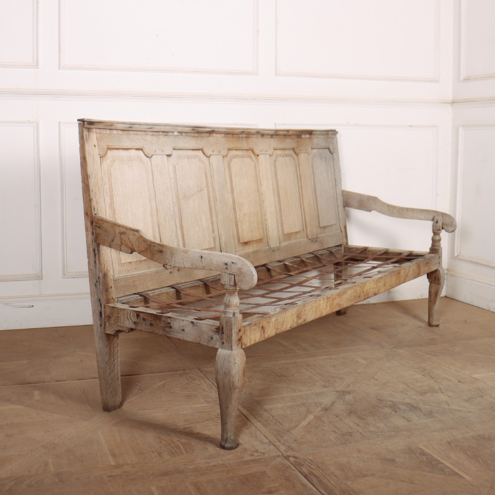 An antique bleached oak settle featuring a high panelled backrest, shaped armrests, turned legs, and a webbed seat base.