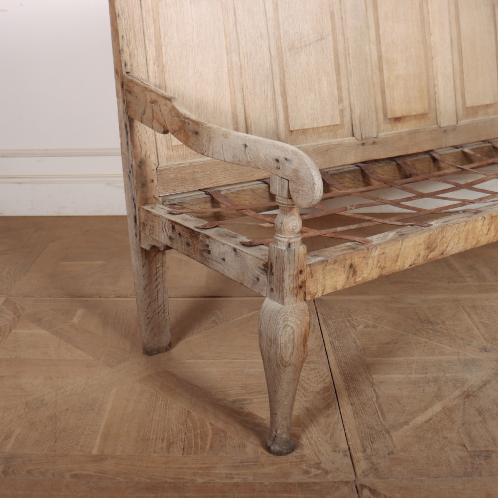 An antique bleached oak settle featuring a high panelled backrest, shaped armrests, turned legs, and a webbed seat base. View III