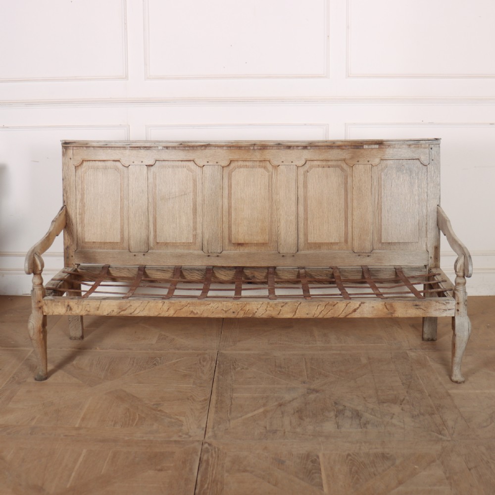 An antique bleached oak settle featuring a high panelled backrest, shaped armrests, turned legs, and a webbed seat base. View IV