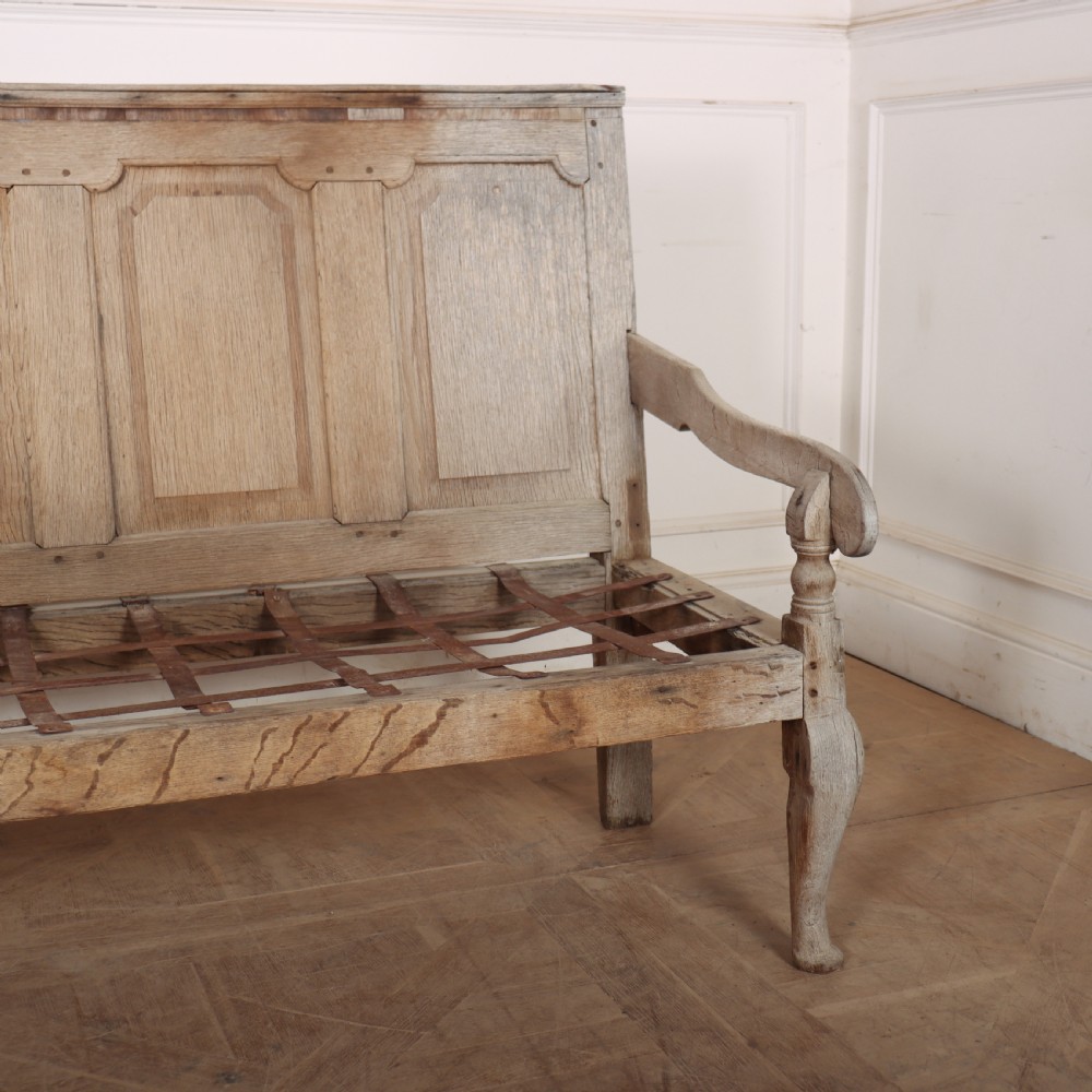 An antique bleached oak settle featuring a high panelled backrest, shaped armrests, turned legs, and a webbed seat base. View V