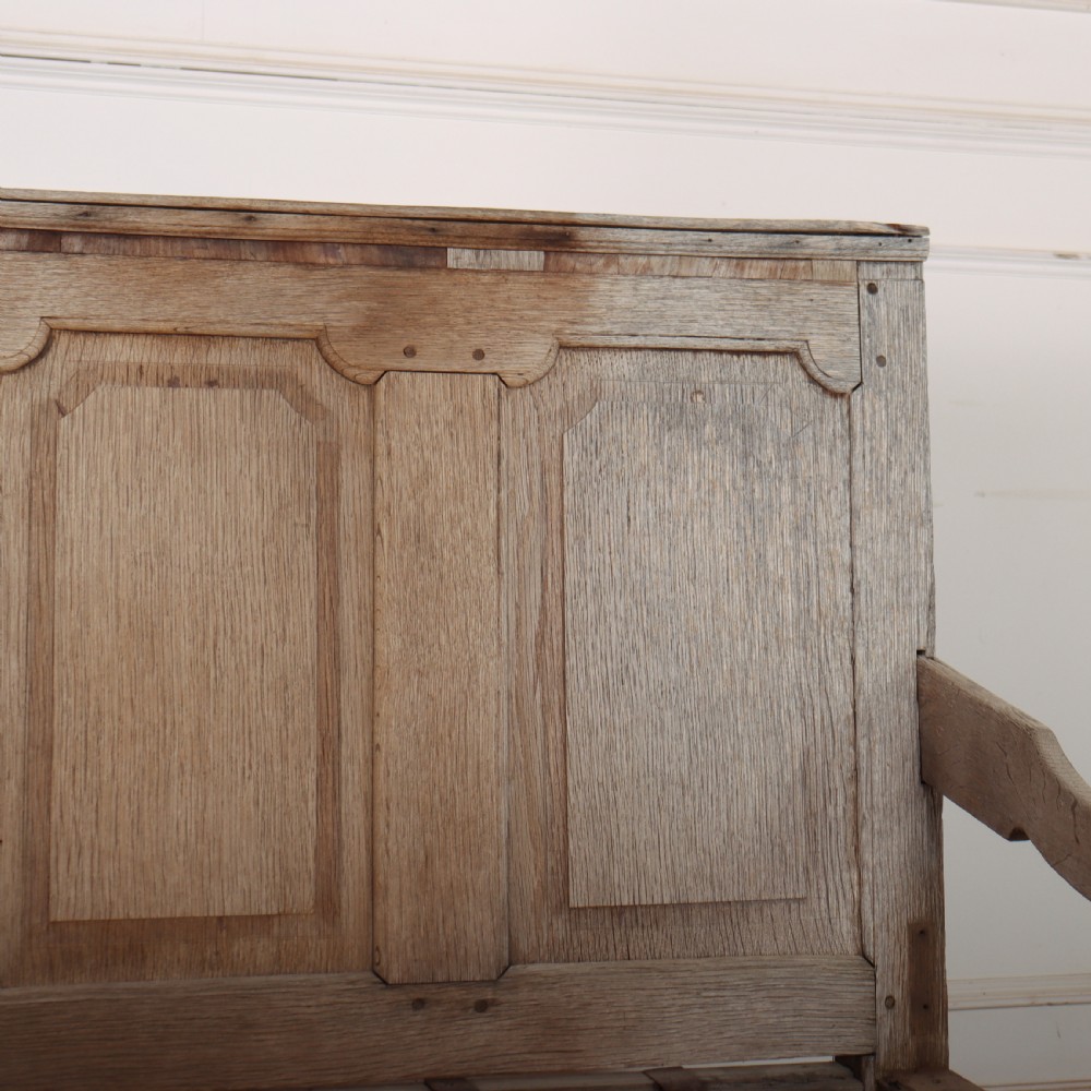 An antique bleached oak settle featuring a high panelled backrest, shaped armrests, turned legs, and a webbed seat base. View VI
