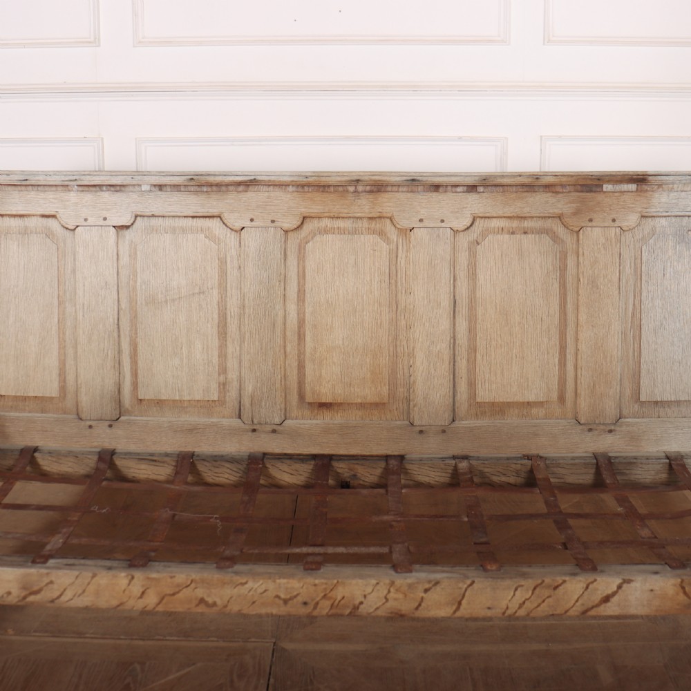 An antique bleached oak settle featuring a high panelled backrest, shaped armrests, turned legs, and a webbed seat base. View VII