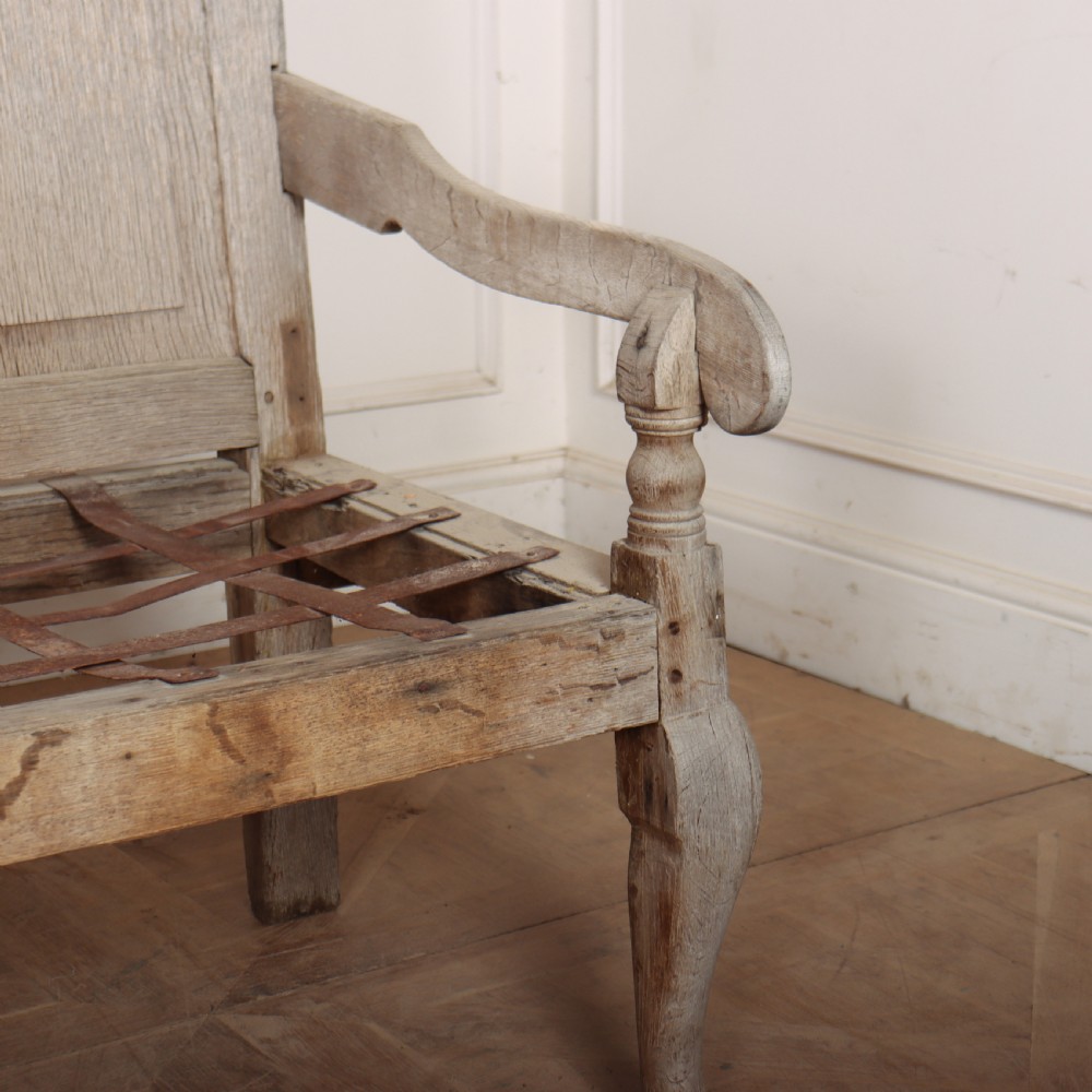An antique bleached oak settle featuring a high panelled backrest, shaped armrests, turned legs, and a webbed seat base. View VIII