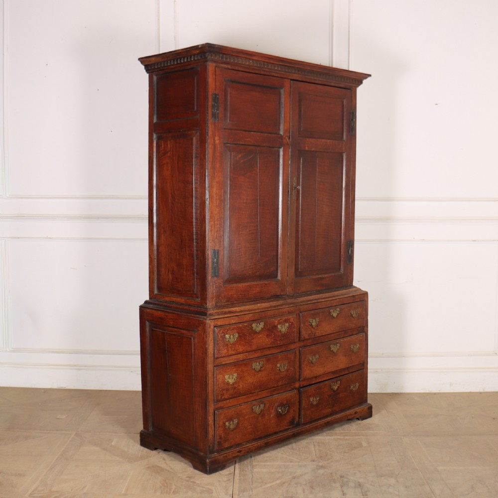 An antique two-part English oak linen press featuring upper fielded panel cupboard doors and a base with six drawers fitted with brass drop handles.