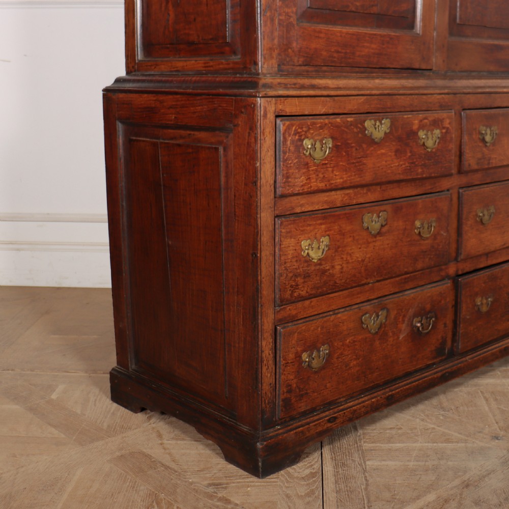 An antique two-part English oak linen press featuring upper fielded panel cupboard doors and a base with six drawers fitted with brass drop handles. View III