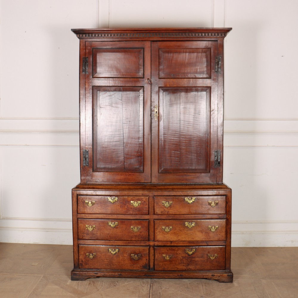 An antique two-part English oak linen press featuring upper fielded panel cupboard doors and a base with six drawers fitted with brass drop handles. View IV